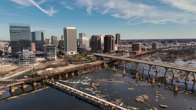 Cinematic aerial view of downtown Richmond Virginia skyline and James River with industrial bridge foreground
