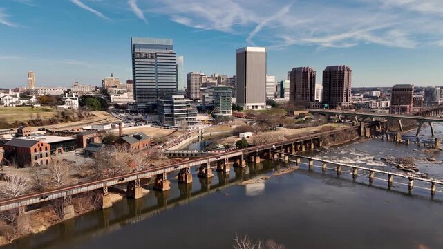 Cinematic aerial view of downtown Richmond Virginia skyline and James River with industrial bridge foreground