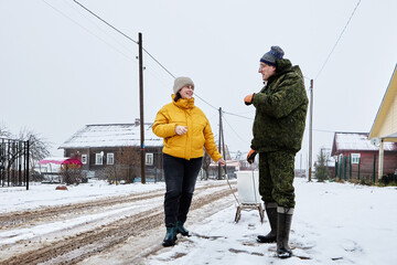 Delivery of garbage to commercial dumpster in rural area in winter, mature couple uses sled.
