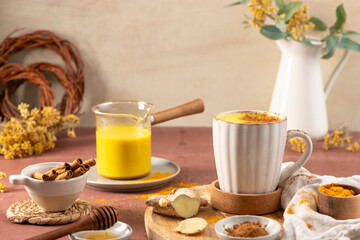 Cozy scene featuring a warm turmeric latte in a ceramic mug alongside fresh ginger root cinnamon...