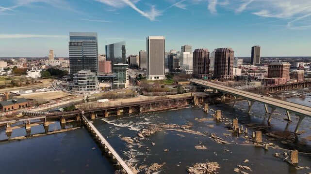 Cinematic aerial view of downtown Richmond Virginia skyline and James River with industrial bridge foreground