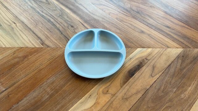 Close up of a hand placing an empty toddler divided plate on a wooden table. Child-friendly dining and parenting lifestyle concept.