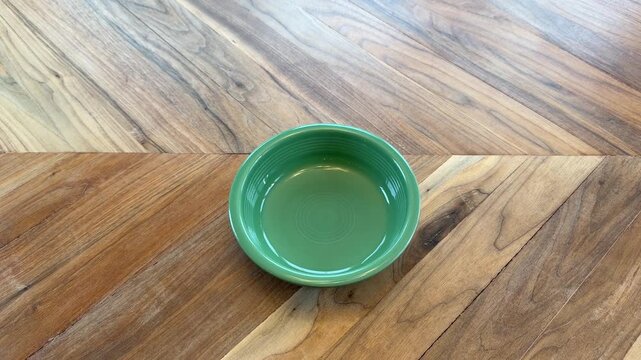 Close up of a hand placing an empty green bowl on a wooden table. Minimal dining and kitchenware concept.