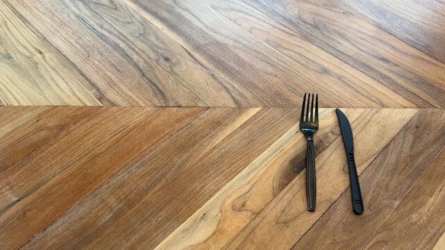 Close up of a plastic fork placed next to a plastic knife on a wooden table. Disposable dining and food service table setting concept.