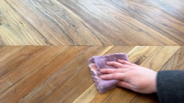 Close up of a hand wiping a wooden table with a microfiber cloth in a circular motion. Everyday home cleaning, surface maintenance, and household hygiene concept.