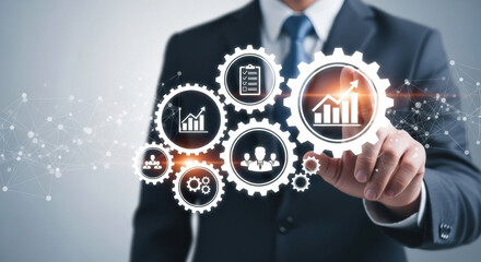 A businessman in a suit touches glowing white gears with embedded chart icons on a gray background, symbolizing business strategy and technological advancement.