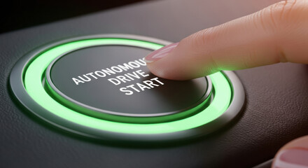 Close up of a finger pressing an 'Autonomous Drive Start' button with a green ring on a black console, illustrating futuristic vehicle technology.