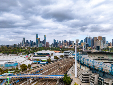 Melbourne's Iconic Sports Precinct and Dynamic City Skyline Under a Cloudy Sky, featuring John Cain Arena and extensive train tracks.