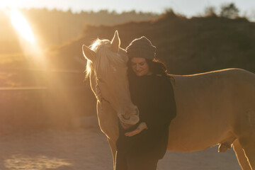 Young woman gently touching her horse outdoors, backlit by golden sunlight, calm rural atmosphere
