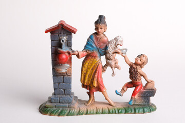 A women pours water from a well for her child and her lamb-figurine