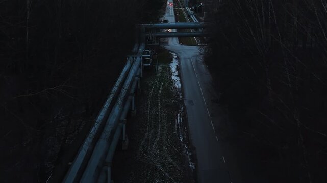 Pipeline intersects tranquil forest pathway during dusk with snow patches and surrounding trees