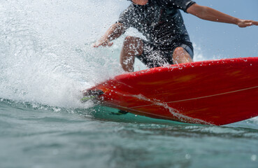 Naklejka premium A young man in a black wetsuit rides a wave on a red surfboard and carves a hard turn in front of the camera.