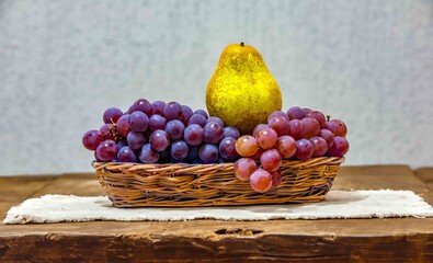 Fresh Grapes and Pear in a Wicker Basket on a Wooden Table. Still life and fine art