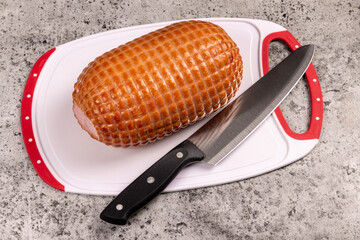 A cooked boneless mini ham lying on a cutting board with a large knife on a grey concrete kitchen counter