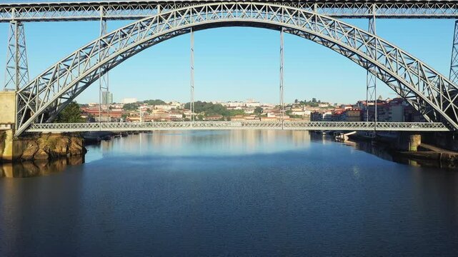 Wide view of the Luis I Bridge spanning the Douro River with the cityscape of Porto, Portugal in the background under clear blue sky.