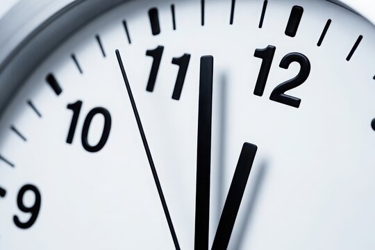 Extreme close up of white wall clock with black hands pointing at twelve o'clock, time management concept