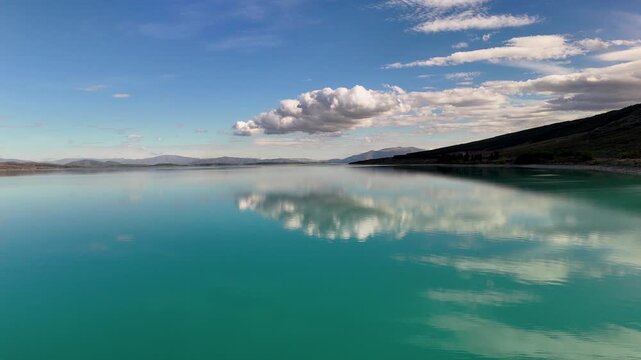 Flying horizontally over lake Pukaki near mt cook in New Zealand with blue water and bright clouds 