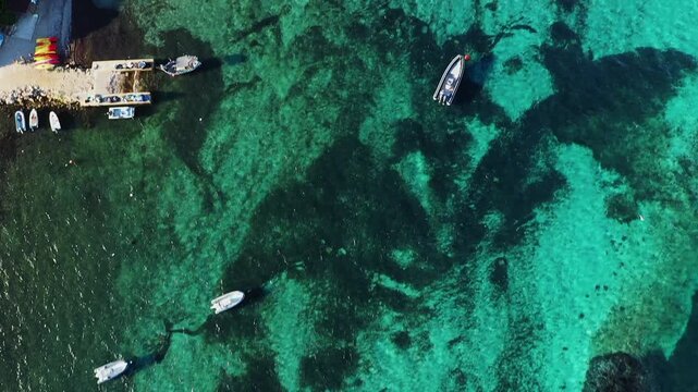 Scenic aerial shot of boats docked at a marina with turquoise waters and lush greenery at Plage du Petit Sperone, Corsica. The vibrant coastal landscape highlights the beauty of this Mediterranean