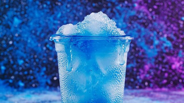 A refreshing icy blue slushy drink with condensation dripping down a transparent plastic cup, set against a vibrant blurred background.