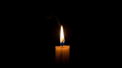 A single burning candle flickers in darkness with smoke rising representing remembrance and solemnity
