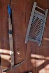 Vintage alpinist ice-axe and old rusty metal sifter in wooden frame, hanged on wooden wall of garden shed. 