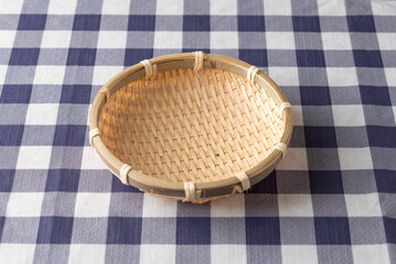 Empty bamboo strainer basket on blue and white checkered tablecloth