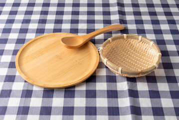 Wooden plate with bamboo strainer basket and spoon on blue checkered tablecloth