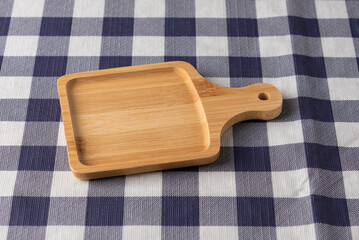 Square wooden serving board with handle on blue and white checkered tablecloth