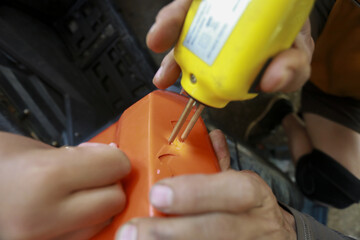 Technician hand repairing broken orange part using yellow hot plastic stapler welding tool in...