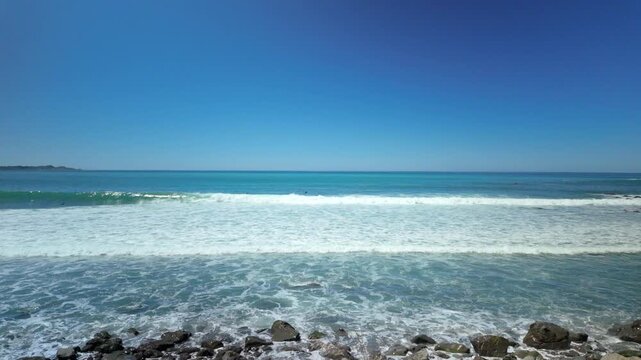Bird flying over ocean surf under clear blue sky