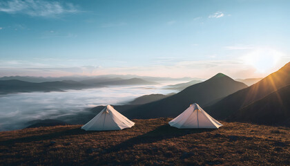 Two white pyramid tents are set up on a grassy mountain peak overlooking a sea of fog at sunrise with sun rays filtering through the distant hazy mountains and a clear blue sky above