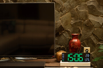 Medium close up of TV set flat screen with digital clock and natural stone wall background