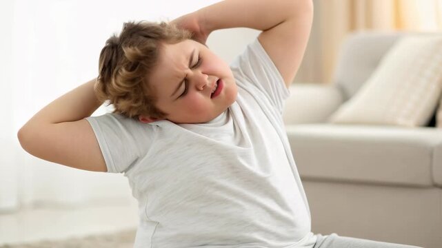 Child boy holding head pain and discomfort living room couch while tired overweight boy stretches behind showing morning sleepy effort and mild