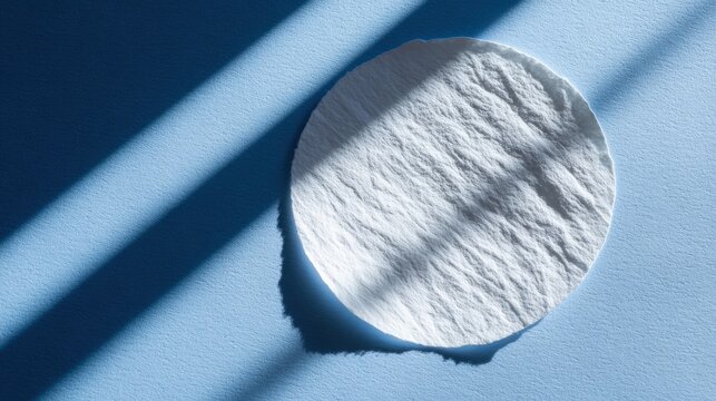 Single round facial cleaning pad rests on textured blue surface illuminated by harsh parallel sunlight.