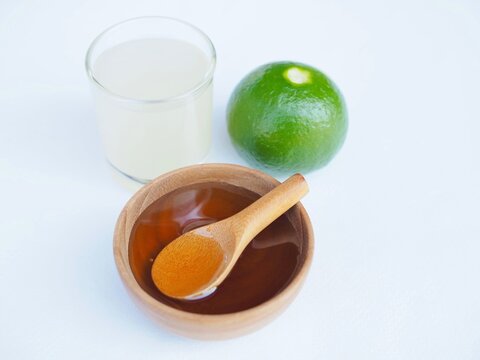 The honey are in a wooden cup, and lemom juice is placed on a white background.