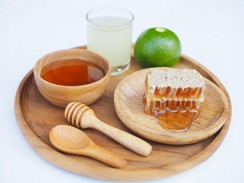 The beehive and honey are in a wooden cup, and lemom juice is placed on a white background.