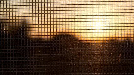 Sunset view through mesh window with silhouetted landscape in warm orange glow