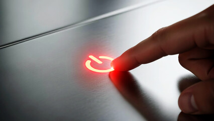 A finger presses a glowing red power button on a sleek surface