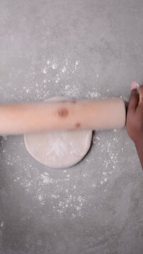 Overhead view of chinese scallion pancake dough being rolled on cement countertop, top view of homemade scallion pancakes, process of making cong you bing