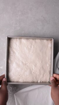overhead view of focaccia dough proofing in baking pan, top view of a high hydration focaccia bread dough resting in a pan, process of making high hydration focaccia