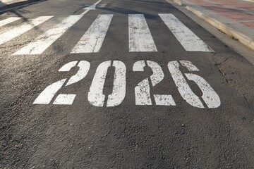 A high-angle view captures the numerical representation of the year 2026 prominently painted directly onto a textured asphalt road surface. The large white stenciled digits, along with the adjacent pe