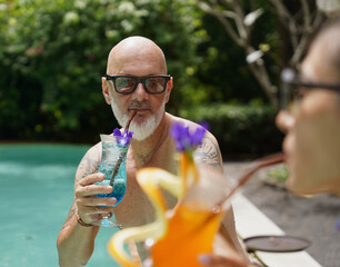 A man and a woman sit by the pool with cocktails and fruit.