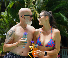 A man and a woman sit by the pool with cocktails and fruit.