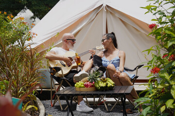 A man plays guitar for a woman near a cozy tent at a glamping site.