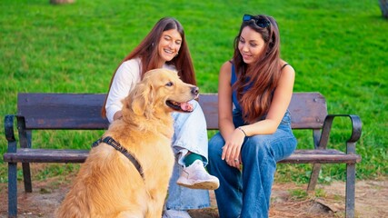 Two women and a golden retriever sitting on a park bench