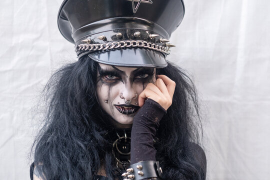 Woman with gothic makeup and piercings wearing black leather cap with spikes looking directly at camera expressing dark power rebellion mystery and intense alternative identity