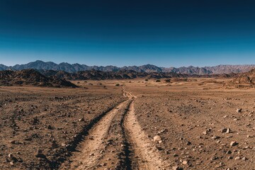 Dirt Road Through Rocky Terrain Landscape Under Blue Sky Scenery Featuring Rugged Mountains, Arid Ground, Remote Travel, Natural Beauty and Warm Colors