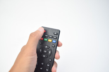 A person's hand holding a black television remote control against a plain white background