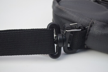 Detailed view of a black plastic swivel snap hook attached to a nylon webbing shoulder strap on a bag