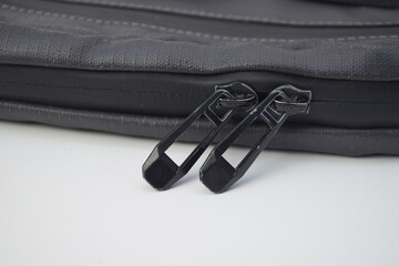 Close-up of two black metal zipper pulls on a grey textile bag. Functional detail of a modern luggage fastener